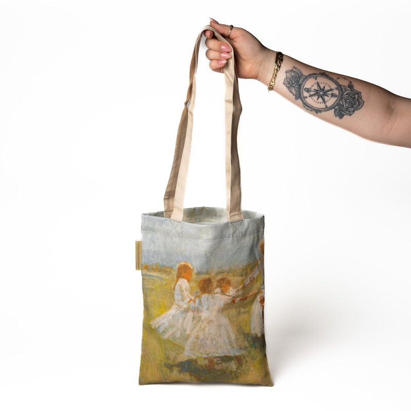 A model's hand is holding a shopping bag printed with the motif Matija Jama’s Kolo