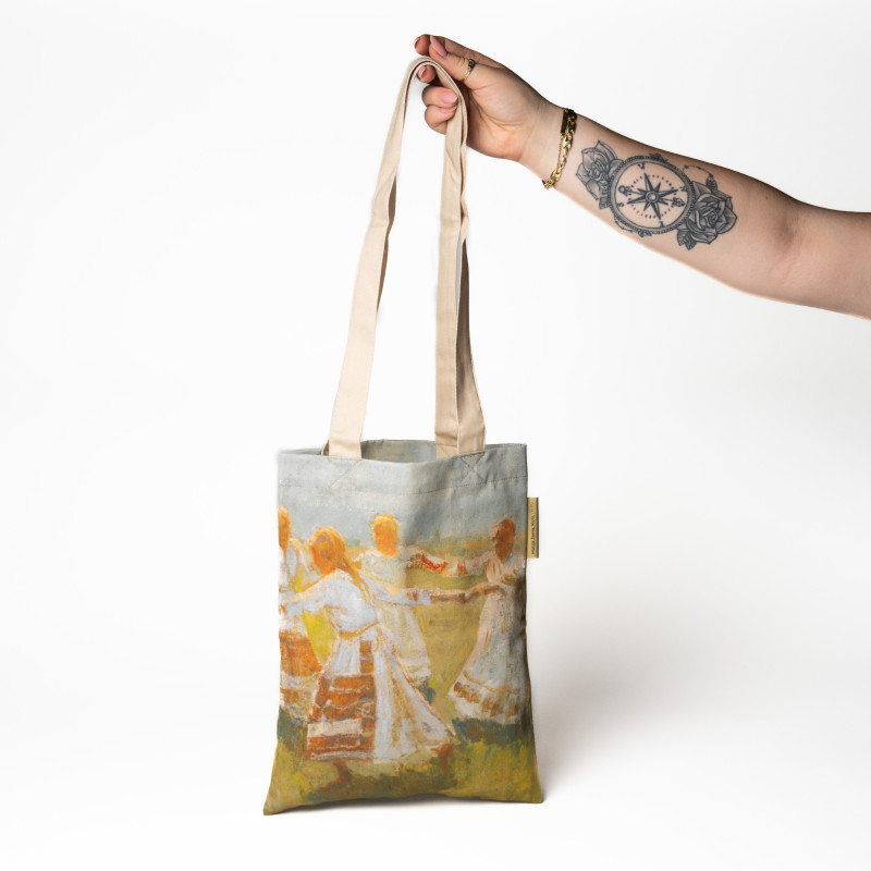A model's hand is holding a shopping bag printed with the motif Matija Jama’s Kolo