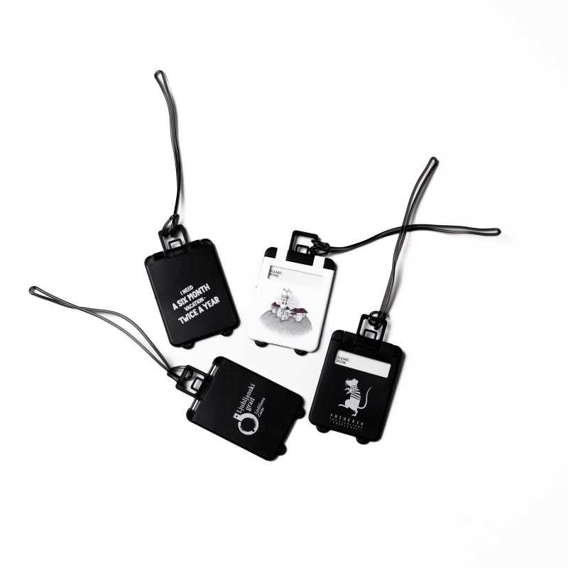 Štirje obeski za prtljago, en v beli barvi in trije v črni, vsi v obliki potovalnega kovčka.