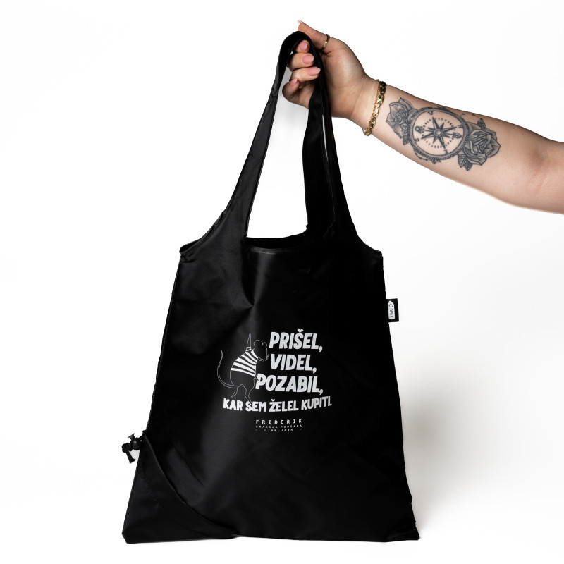 Roka modela drži črno vrečo. Na vreči je bel potisk besedila v slovenščini.